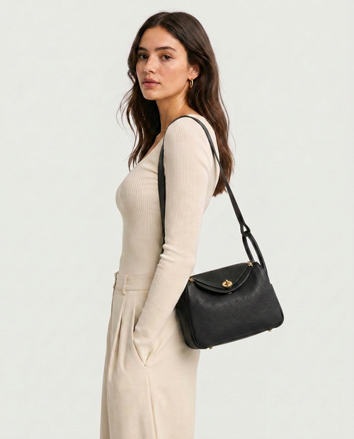 Model carries the black Cora vegan leather bag on one shoulder, with front flap and gold-tone lock visible